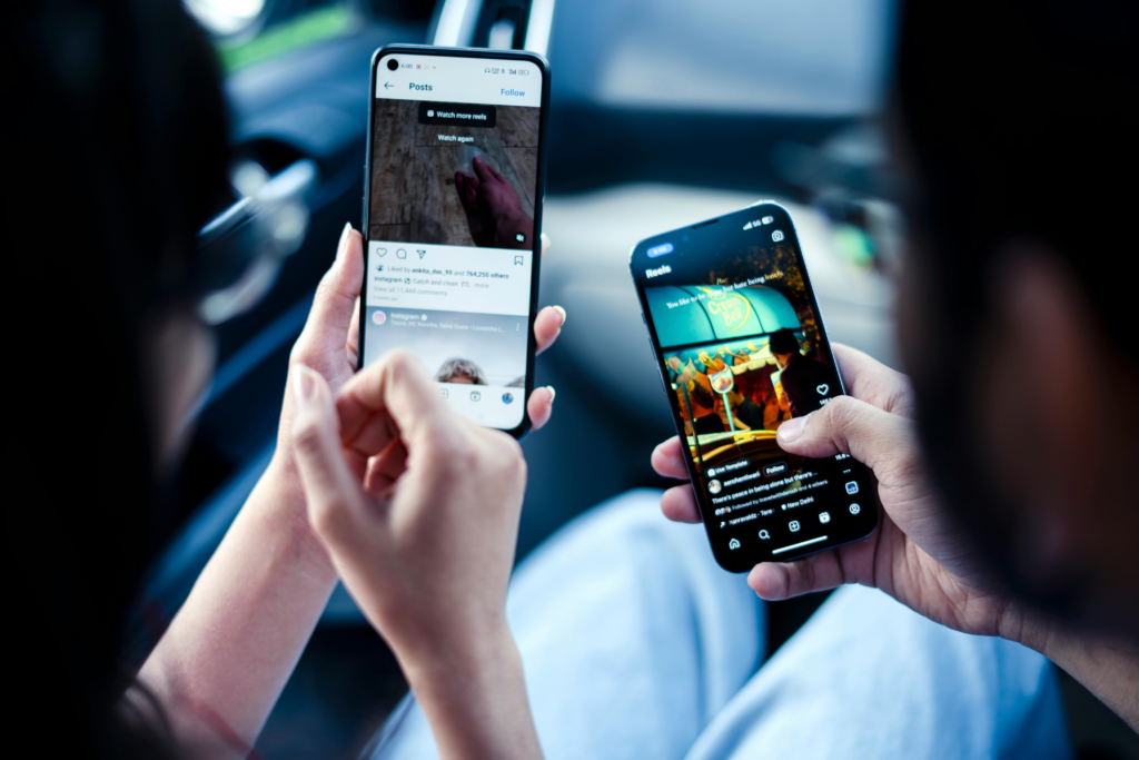 Two people in the foreground hold out cell phones and are looking at social media posts.